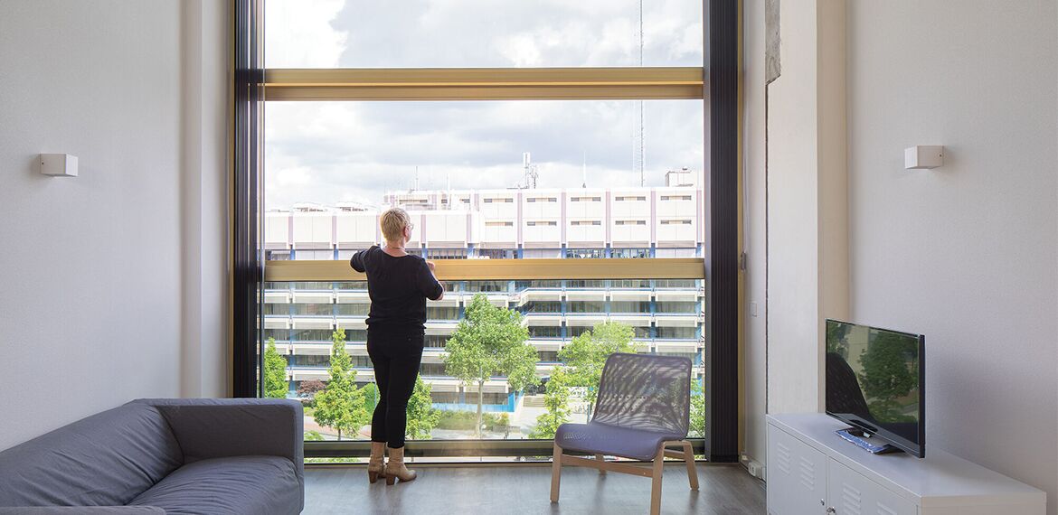 Een vrouw kijkt uit een groot Reynaers Aluminium raam in het Philips Lighting gebouw.
