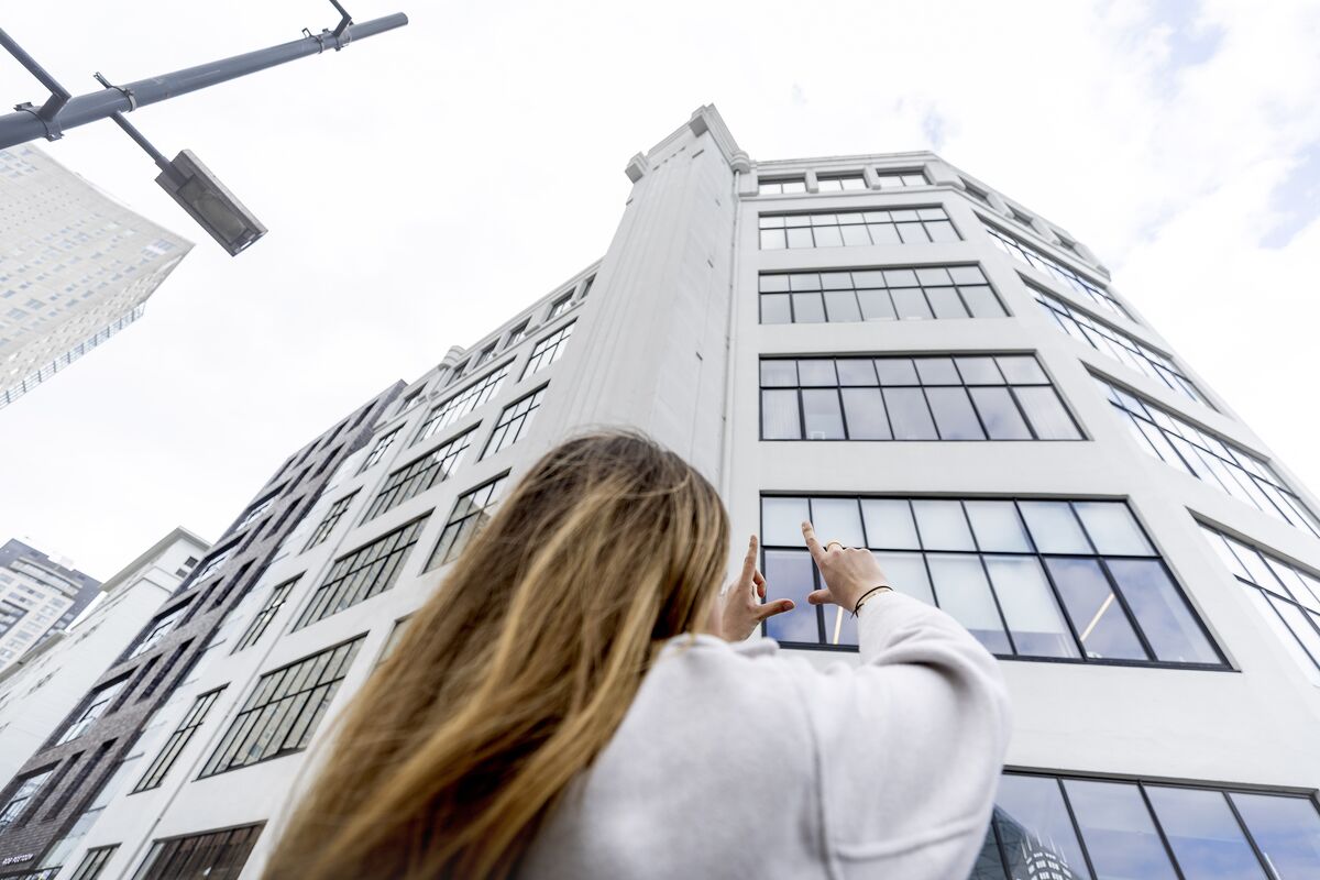 Vrouw houdt haar handen omhoog in de richting van een wit flatgebouw met veel ramen.