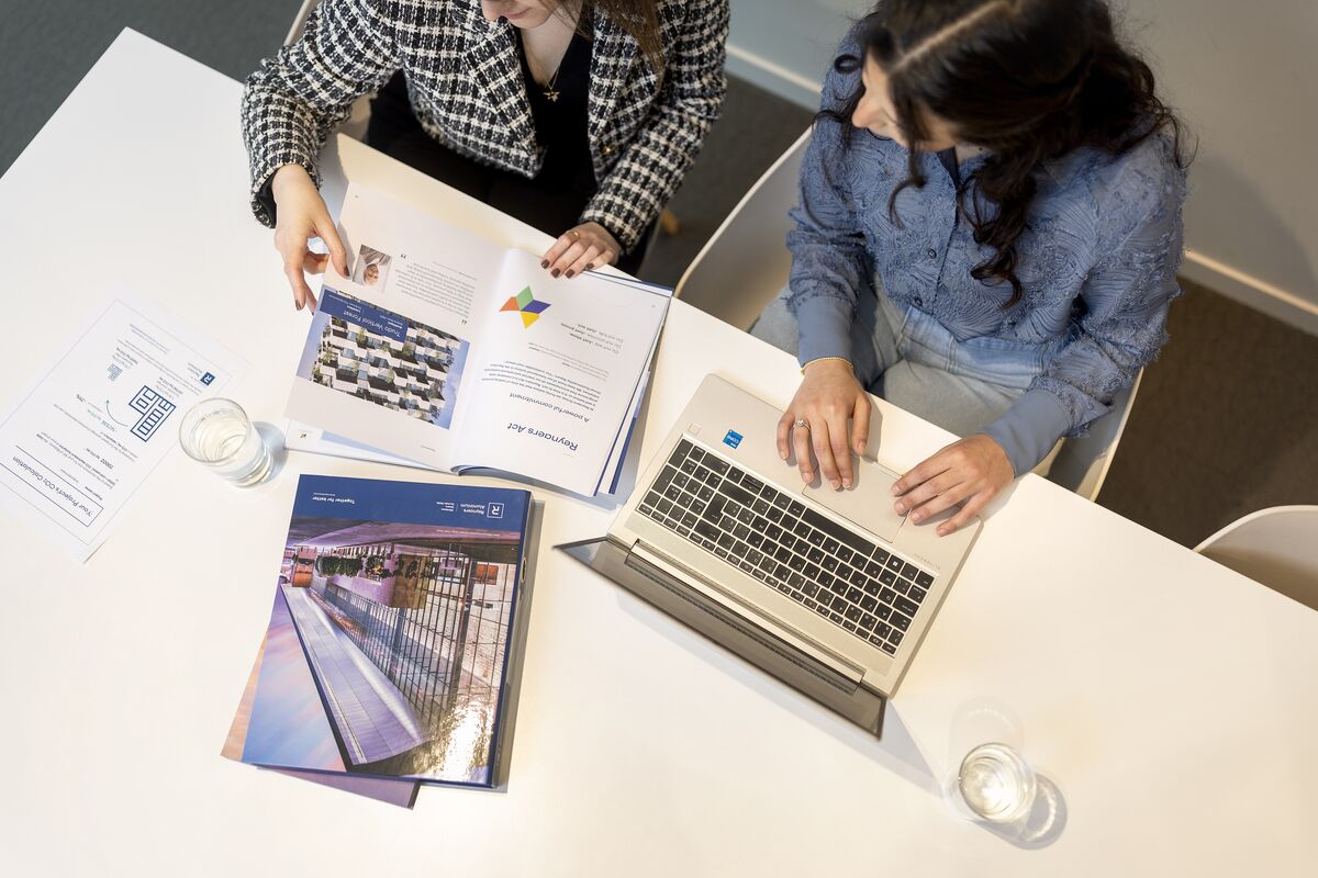 Bovenaanzicht van bureau met papieren, laptop en mappen.