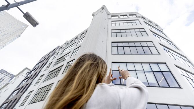 Vrouw houdt haar handen omhoog in de richting van een wit flatgebouw met veel ramen.