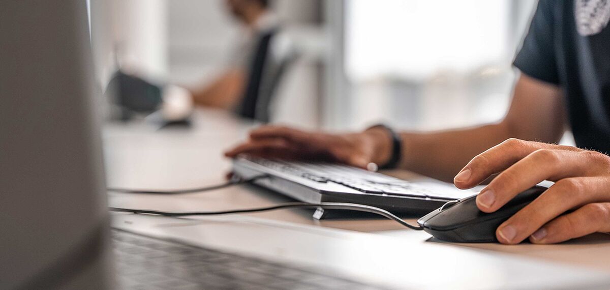 Reynaers Aluminium employee using a mouse and keyboard at his desk.