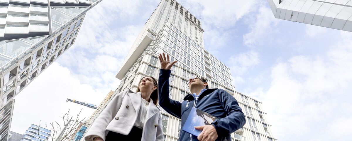 Man en vrouw voor wolkenkrabber wijzen naar de lucht