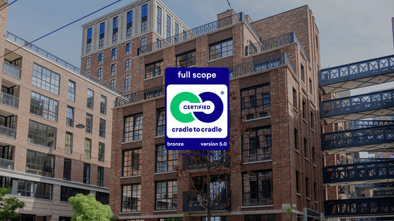 The Cradle to Cradle logo in front of red brick mid-rise buildings.
